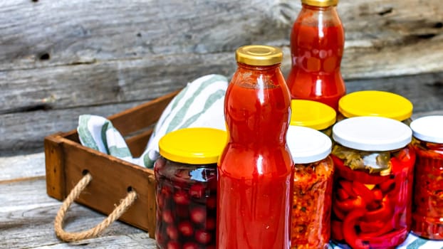 Jars with variety of canned vegetables and fruits, jars with zacusca and bottles with tomatoes sauce. Preserved food concept in a rustic composition.