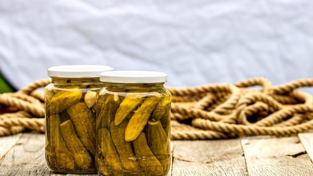 Glass jars with pickled red bell peppers and pickled cucumbers (pickles) isolated. Jars with variety of pickled vegetables. Preserved food concept in a rustic composition.