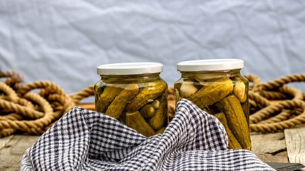 Glass jars with pickled red bell peppers and pickled cucumbers (pickles) isolated. Jars with variety of pickled vegetables. Preserved food concept in a rustic composition.