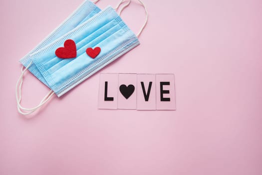 Disposable medical mask and two hearts. Having a baby during the coronavirus pandemic. The inscription love on a pink background