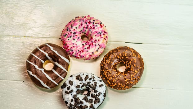 Colorful donuts on white wooden table. Sweet icing sugar food with glazed sprinkles, doughnut with frosting. Top view with copy space