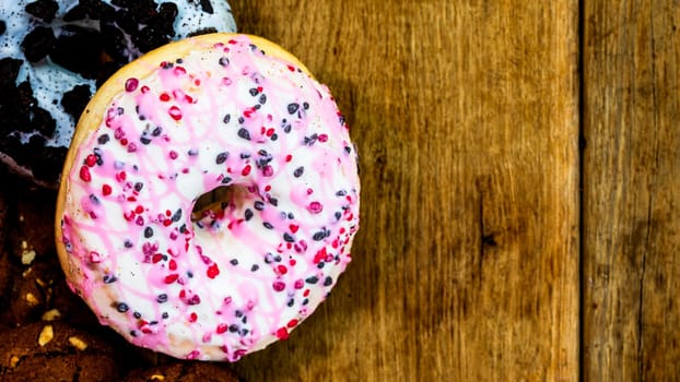 Colorful donuts on wooden table. Sweet icing sugar food with glazed sprinkles, doughnut with chocolate frosting. Top view with copy space