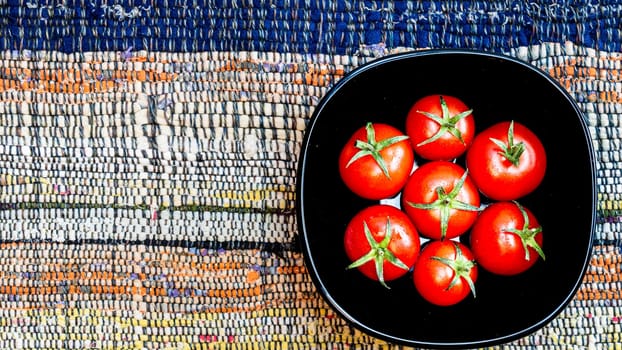 Top detail view of fresh ripe cherry tomatoes in a black bowl on a rustic napkin. Ingredients and food concept