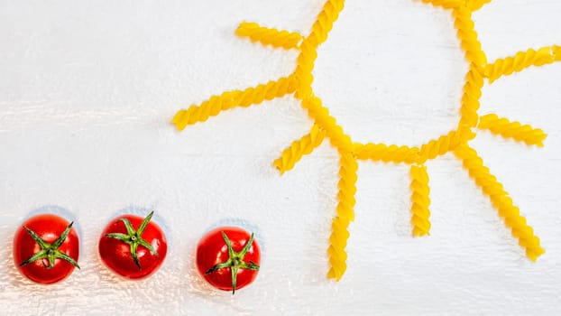 Sun made from fusilli pasta, green field made from green spiral pasta and cherry tomatoes, concept of growing of tomatoes on white background