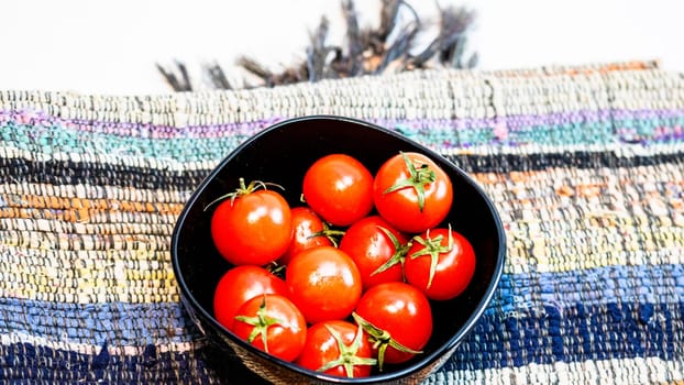 Detail of ripe cherry tomatoes in small black bowl on a rustic napkin. Ingredients and food concept