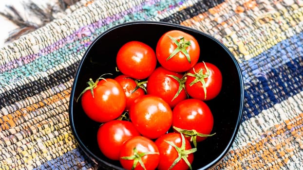 Detail of ripe cherry tomatoes in small black bowl on a rustic napkin. Ingredients and food concept