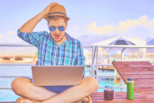 Concept of relaxing at sea. The man is working on time. The amazing face of the worker, in the computer. Shocked