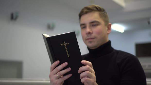 A young man reads the Bible while sitting on a church bench. A Protestant man reads the Bible in church. 4k