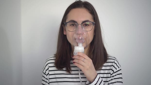 A young woman breathes through an inhaler mask closeup. A girl in glasses with an oxygen mask is being treated for a respiratory infection. 4k