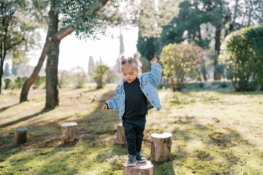 Little girl jumping on tree stumps balancing with her arms in the garden. High quality photo