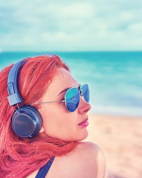 Cool woman listening to music on the beach. The girl enjoys a beautiful view of the sea and listens to music.