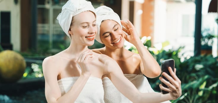 Couple of young beautiful women with beautiful skin in white towel taking a photo together at outdoor surrounded by peaceful natural environment. Beauty and healthy spa concept. Tranquility.