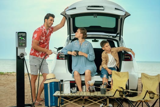 Family vacation trip traveling by the beach with electric car, happy family recharge EV car, enjoying outdoor camping coffee. Seascape travel and eco-friendly car for clean environment. Perpetual