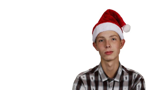 Cute, happy, cheerful teenage boy in a shirt, wearing a Santa Claus hat, on a white isolated background.
