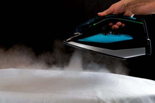 Woman ironing a white cloth by pouring steam from the iron on a black background.