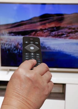Woman with a remote control in her hand changing the television channels in the background a television is on
