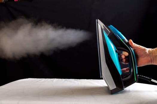 Woman ironing a white cloth by pouring steam from the iron on a black background.