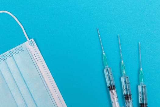 Several Syringe and Face Mask on Blue Table - Top View. Syringes are Prepared for Vaccination or Injection. Medical Experiment. Blue Disposable Medical Mask. Virus protection - Flat Lay