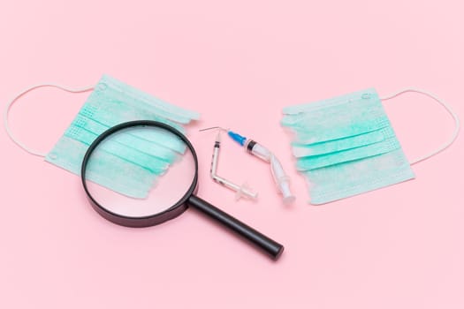 Anti Vaccine Movement and Anti Mask Concept - Broken Medical Syringe and Green Torn Medical Face Mask with Magnifying Glass on the Pink Background. Pandemic and Lockdown End - Top View, Flat Lay