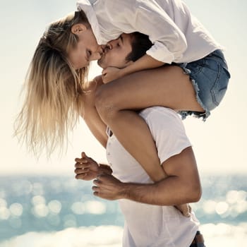 Kiss, love and beach piggyback by couple in nature with support, trust and security outdoor. Romance, care and people at the ocean for shoulder ride, moment or travel, freedom or Bali summer vacation.