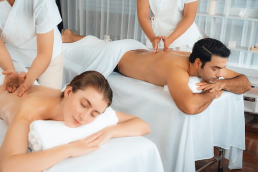 Caucasian couple customer enjoying relaxing anti-stress spa massage and pampering with beauty skin recreation leisure in day light ambient salon spa at luxury resort or hotel. Quiescent