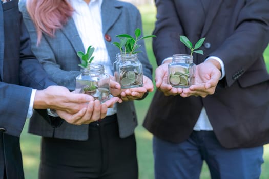 Concept of sustainable money growth investment with glass jar filled with money savings coins with businesspeople as eco-friendly financial investment nurtured with nature and healthy retirement. Gyre