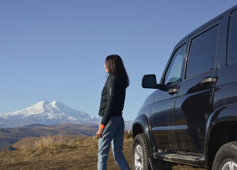 Travel concept. A brunette woman near a large SUV enjoying the views of the Caucasus Mountains