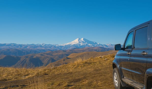 A car against the backdrop of a beautiful landscape, snow-capped Mount Elbrus and blue sky on autumn days.