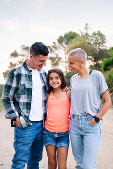 vertical photo looking at camera of a father, mother and daughter smiling happy in the countryside, concept of active tourism in nature and family outdoors activities, copy space for text