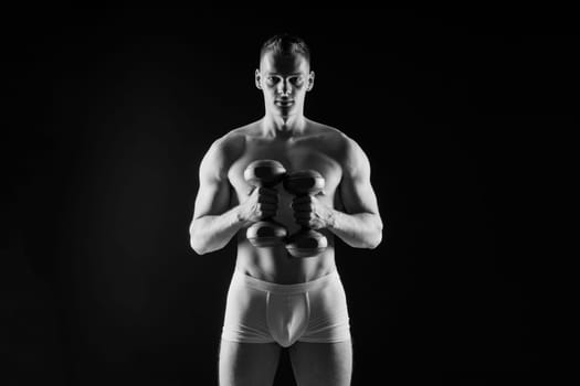 Studio shot of a muscular young man exercising with dumbbells against grey and black background.