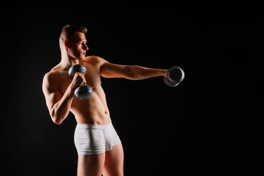 Studio shot of a muscular young man exercising with dumbbells against grey and black background.