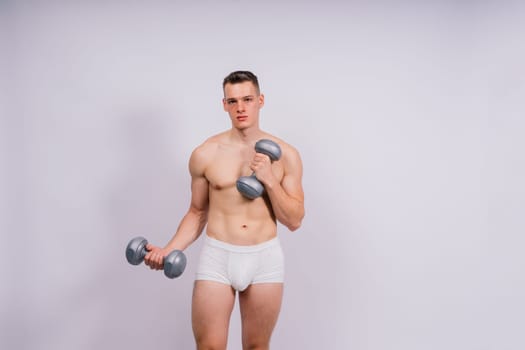 Studio shot of a muscular young man exercising with dumbbells against grey and black background.