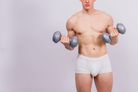Studio shot of a muscular young man exercising with dumbbells against grey and black background.