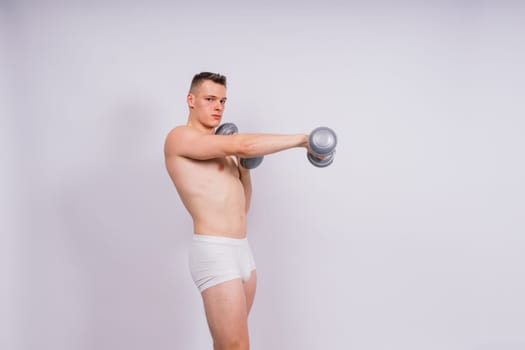 Studio shot of a muscular young man exercising with dumbbells against grey and black background.