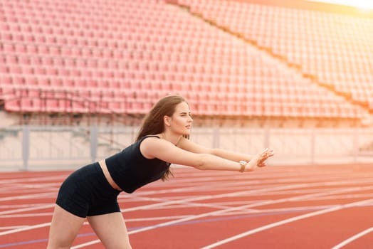 Young, beautiful girl athlete in sportswear is training and running, stretching at the stadium