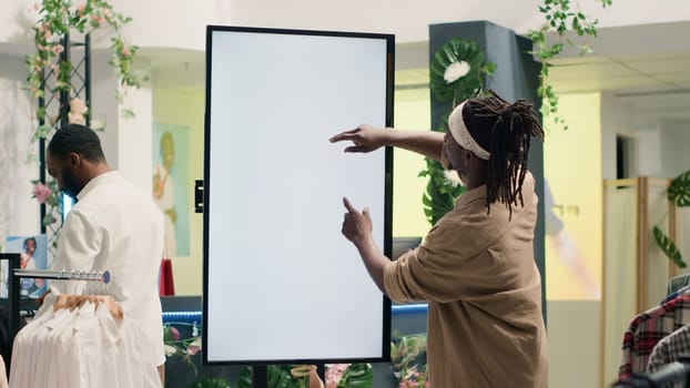 African american man in clothing store using augmented reality mockup screen to look at garment options to try on. Customer using led display to visualize fashion choices in showroom