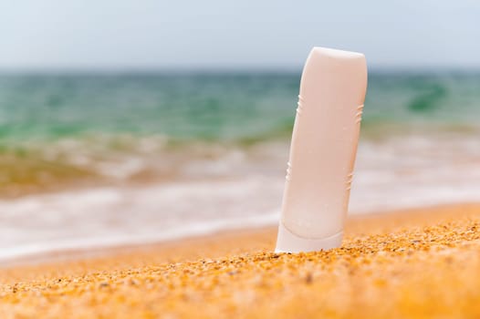 Bottle with sunscreen lotion on the beach, background of sea sky and waves, close-up. Layout for advertising a beauty product.