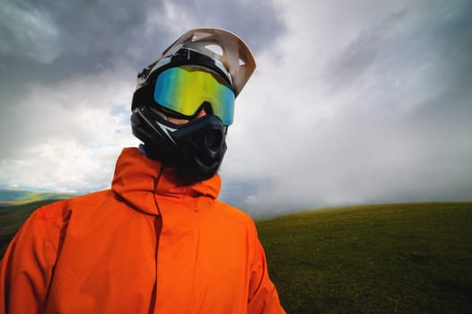 A rider in a helmet and goggles, full protective equipment on an MTB bicycle or motorcycle stands on a rock against the backdrop of hills and low clouds