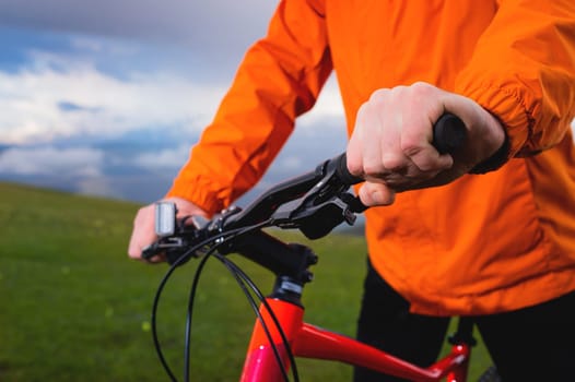 Close up, hands of a cyclist on the handlebars of a mountain bike on a green natural background and cloudy sky. Taking a break while riding a dirt bike.