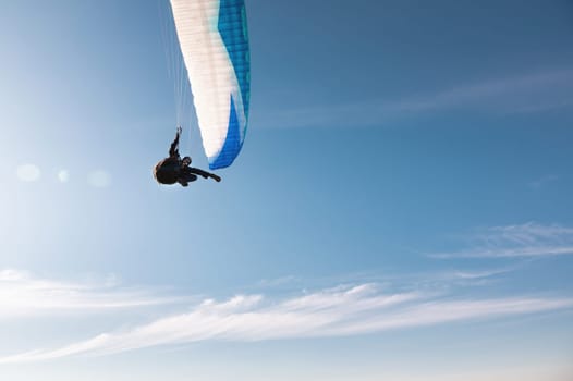 An athlete flies on a paraglider. Beautiful paraglider in flight on a blue sky with white clouds on a sunny day
