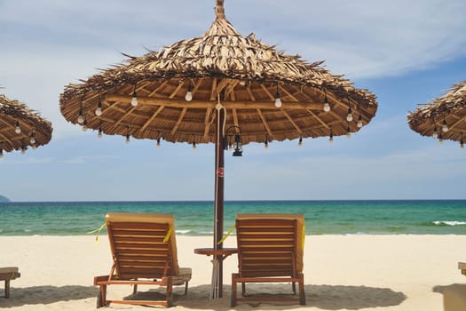 Straw sunshades and sunbeds on the empty pebble beach with sea in the background. Deserted beach with rattan sun loungers and umbrellas