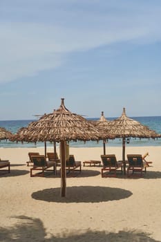 Straw sunshades and sunbeds on the empty pebble beach with sea in the background. Deserted beach with rattan sun loungers and umbrellas