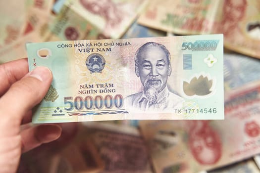 Male hand holds a fan of Vietnames Dong banknote, the currency of Vietnam. Close up Polymer Money of Vietnam. 500000 Dong or VND in male hand. In front a portrait of Ho Chi Minh. Plastic banknotes. High quality photo