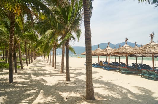 Straw sunshades and sunbeds on the empty pebble beach with sea in the background. Deserted beach with rattan sun loungers and umbrellas