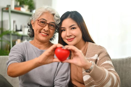 Beautiful middle age mother and daughter holding red heart. Health care, insurance and world heart day concept.
