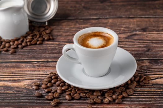 Espresso macchiato in white porcelain cup with milk and coffee beans on wooden table