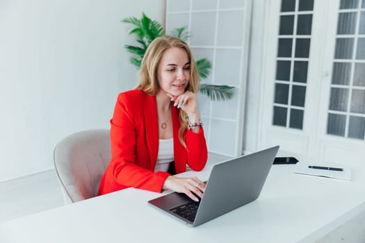 Side view of smiling woman sitting by the table with laptop in office