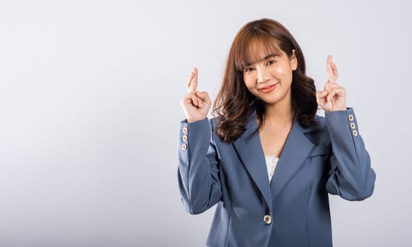 Superstition meets joy in this studio shot of a cute Asian lady. She holds crossed fingers, symbolizing hope and positivity. Isolated on a white background, her expressive face shines with happiness.