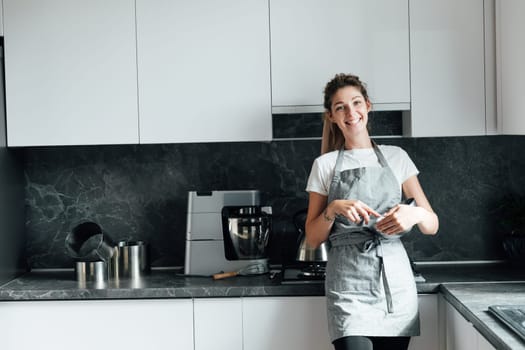 woman in an apron stands in the kitchen and cooks food in a bowl