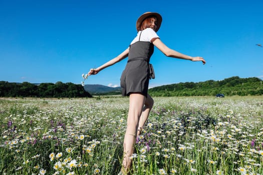 in nature, woman in a straw hat runs into a field with daisies flowers